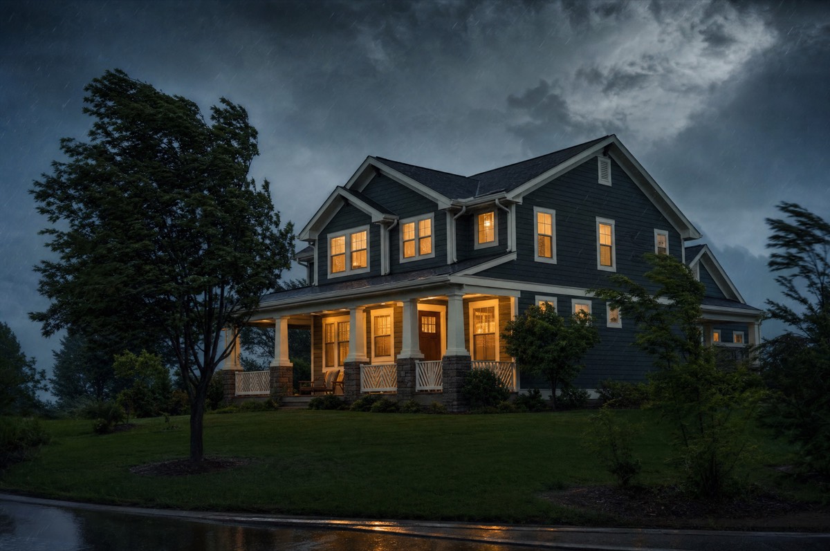 Solid American home standing firm through a storm with warm lights glowing, structural strength