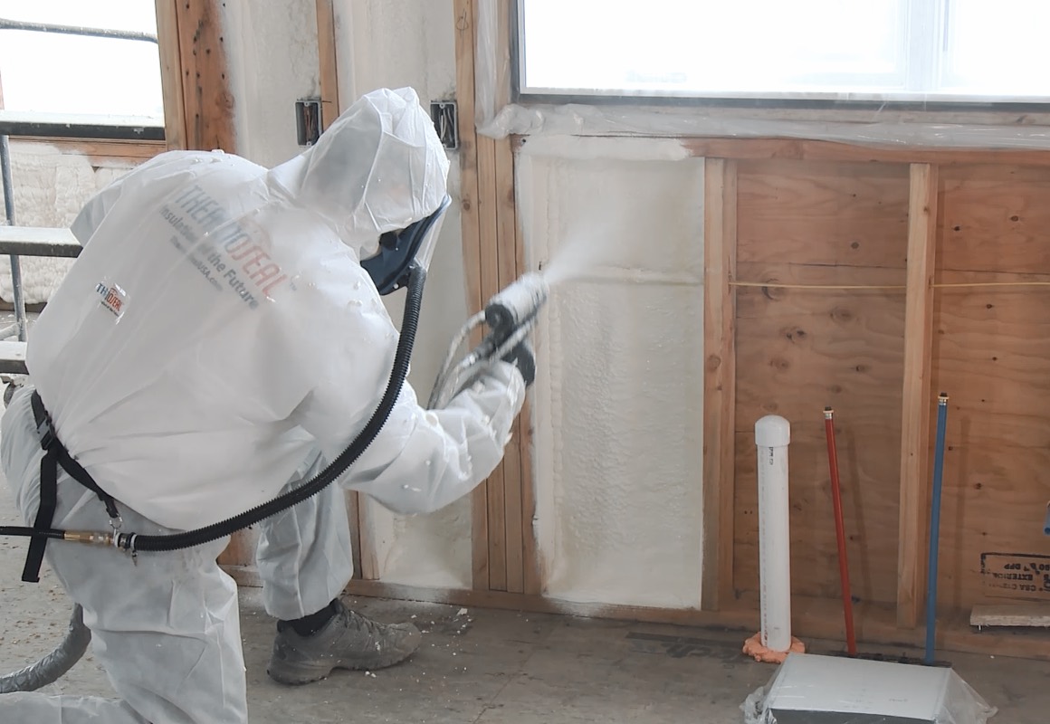 ThermoSeal certified installer in a branded protective suit spraying HFO closed cell foam into wall cavities